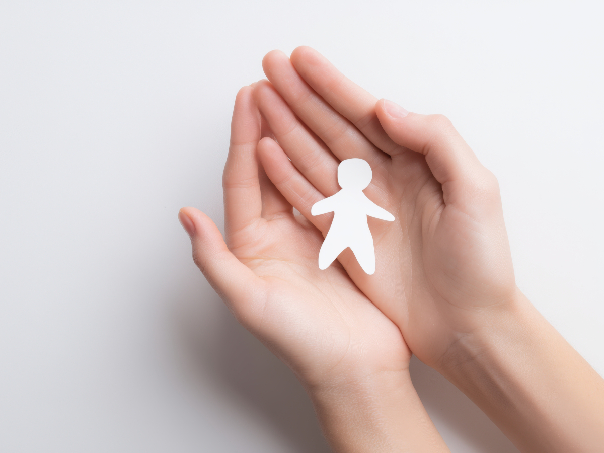 Symbolbild Fehlgeburt, ineinandergefaltete Hände mit Papiermänchen in der Mitte